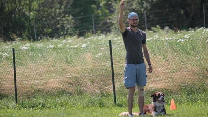 Hundeführer gibt Startsignal, während der Hund bereit für die Stöbersuche auf der Wiese liegt